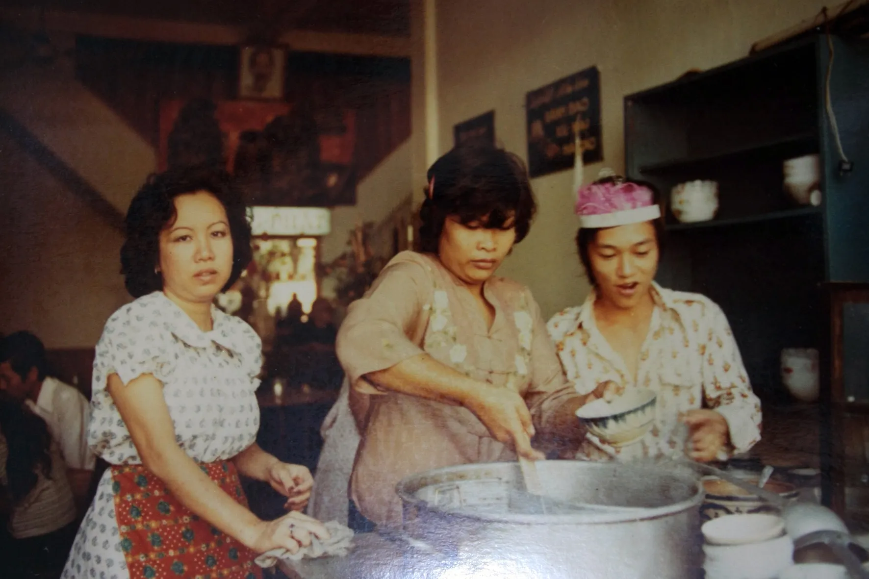 Three women behind the counter, one ladling from a large pot of broth