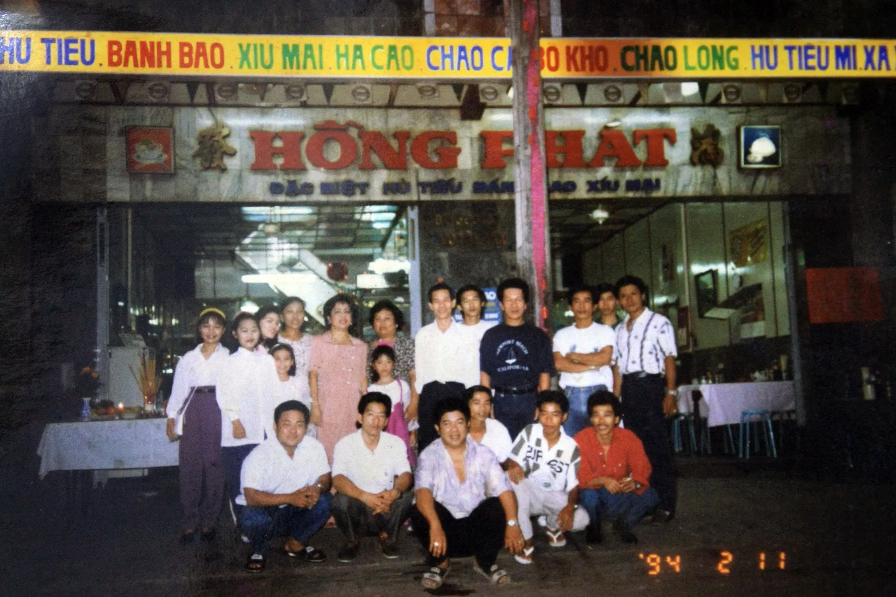 Staff and family gathered at night beneath the lit Hồng Phát sign, in a photo date-stamped 1994